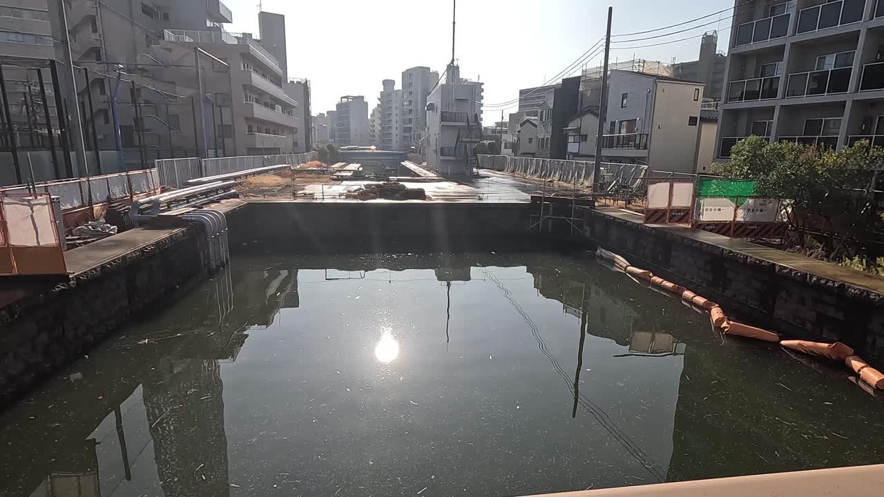 A serene view of a river in Tokyo with surrounding urban architecture, captured under bright sunlight with reflections on the water