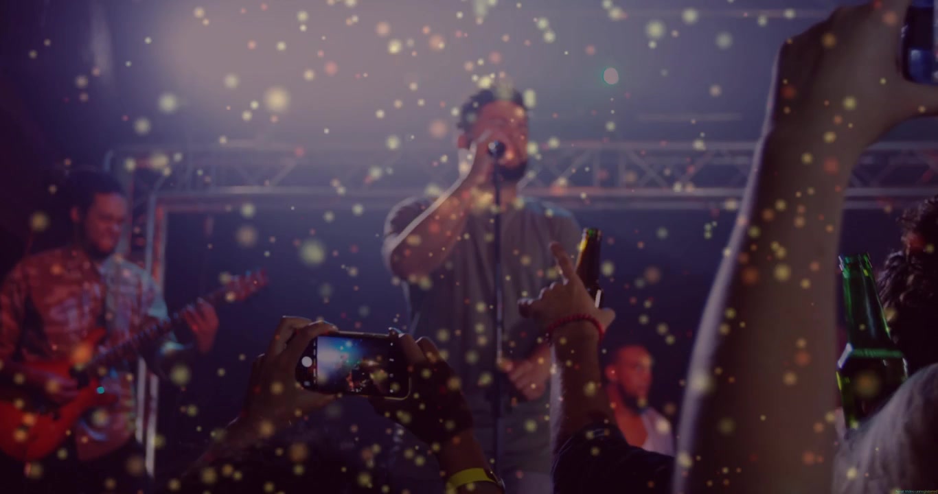 Chanteur commençant une chanson sur scène, foule levant des téléphones, enregistrant tandis que des paillettes dorées flottent au-dessus des téléphones