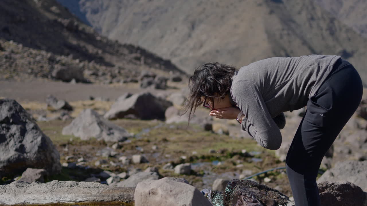 Slow motion of a woman hiker drinking from a water source high up in rocky ATLAS mountains