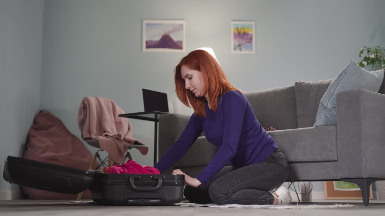 mujer pelirroja abre una maleta negra después de llegar a casa