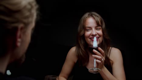a woman grins at a man while sipping red wine - close up