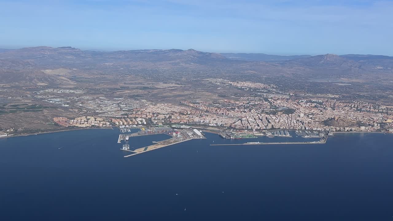 Aerial left side view of Alicante city center and harbor, taking from a plane cokpit in a sunny day. Handheld camer shot from cokcpit