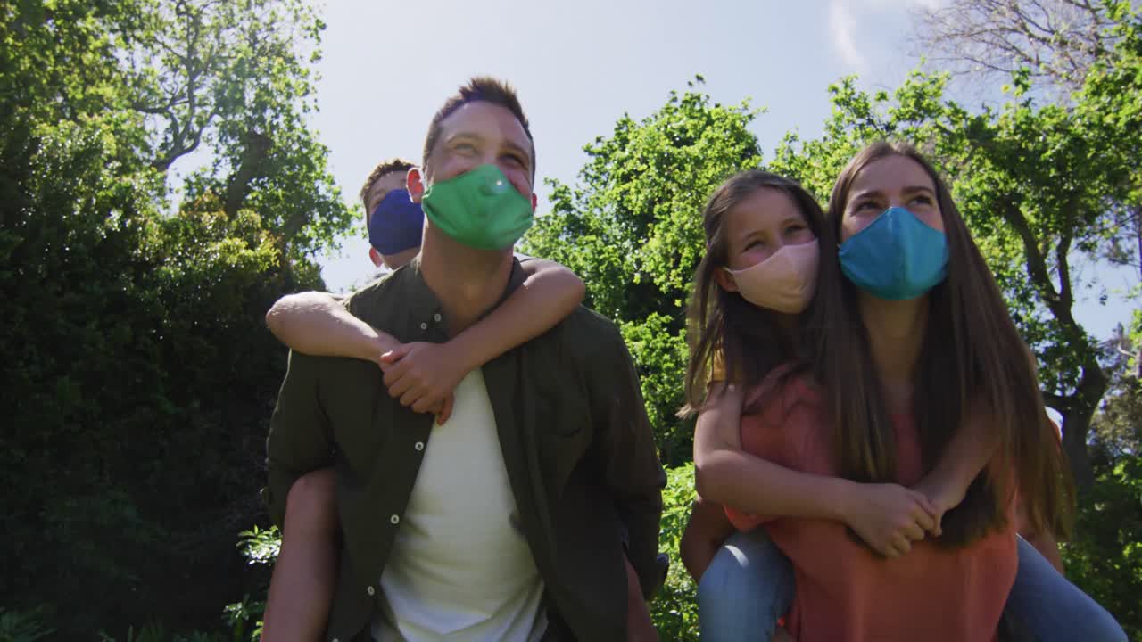 백인 부부가 마스크를 쓰고 정원에서 아들과 딸을 등에  ⁇ 고 있습니다.