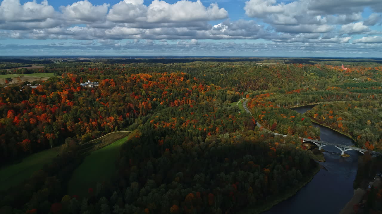 The autumn season's breathtaking landscape, captured from a drone hovering above the picturesque lake adorned with a mesmerizing bridge and enchanting forest, is enhanced by the milky white clouds