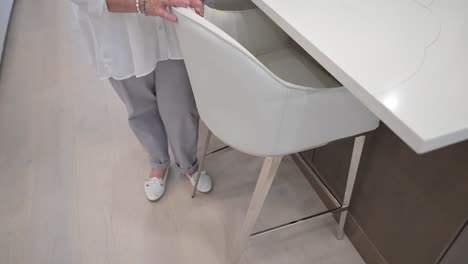 older woman smiles contently while in the kitchen at the corner of a white marble countertop and fruit