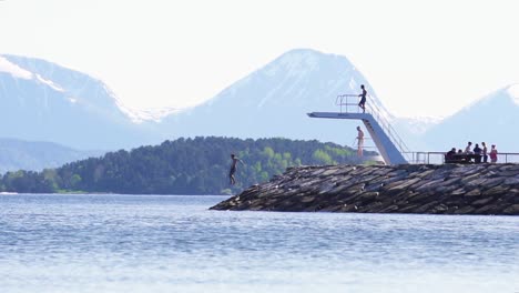 slow motion shot of a person jumping off of a diving board into the sea, water splashing up. beautiful scenic mountain view in the background. molde, norway.