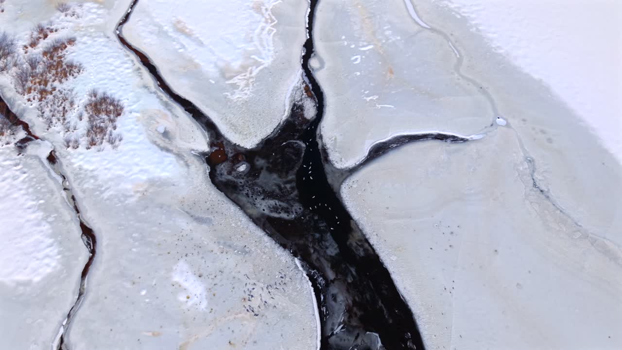 Una vista dall'alto su un lago ghiacciato con ruscelli e affluenti non ghiacciati in una giornata di sole d'inverno. La neve sul lago e l'acqua sembrano marmo mentre la telecamera si è inclinata verso il basso, ha fatto uno zoom in avanti e si è abbassata con un movimento a gru