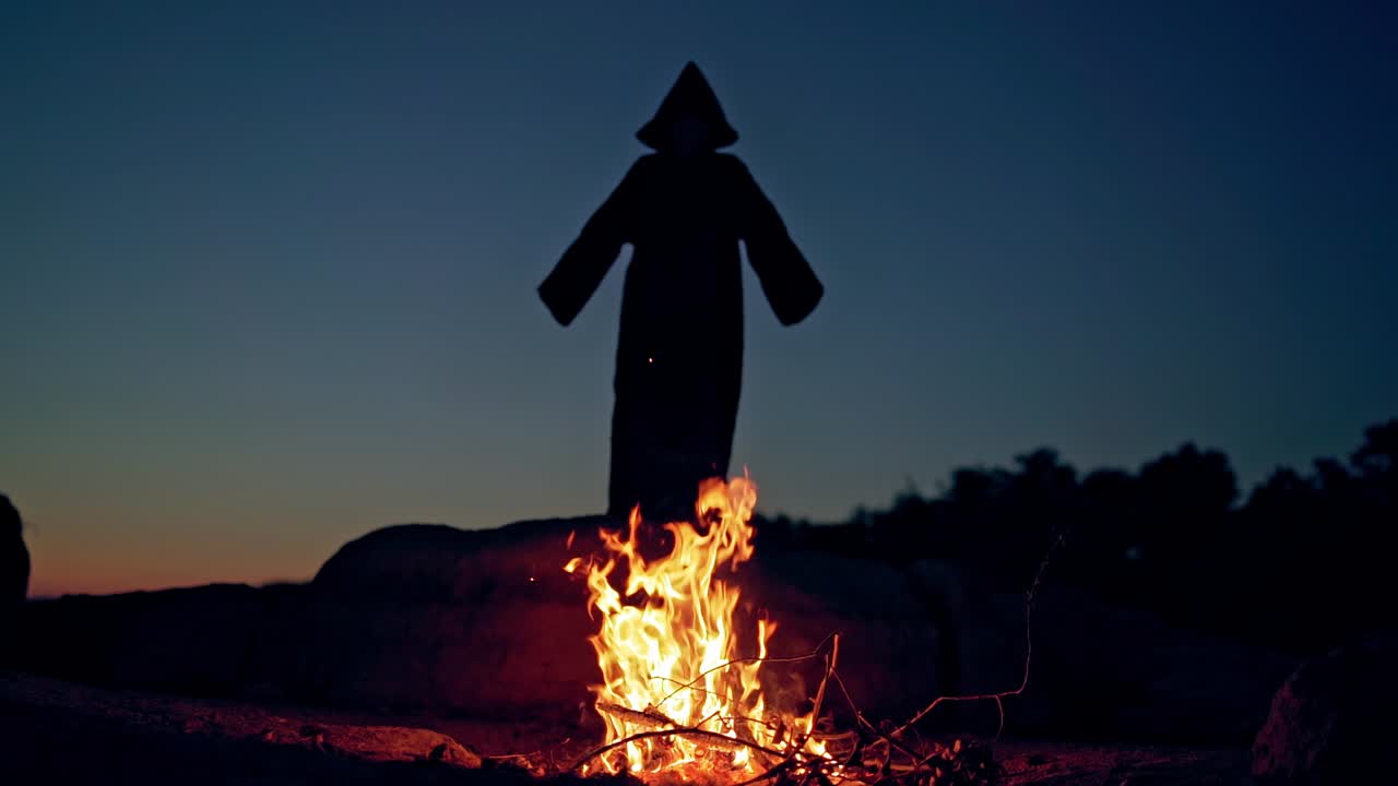 Horrible atmosphere at night in nature. Silhouette of death against the fire. Black figure of devil.