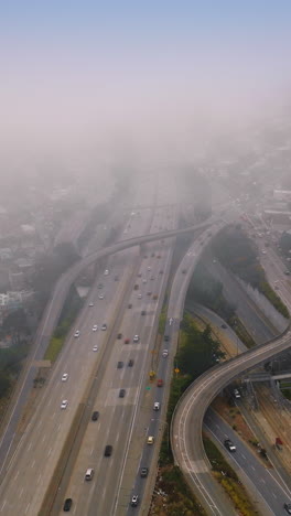 wavy complicated roads going to the thick fog. numerous cars riding by the highways on foggy daytime. top view. vertical video