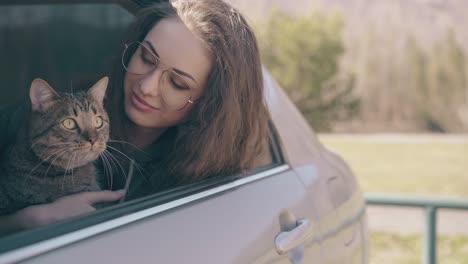 chica feliz con un gato lindo se sienta en el auto contra el prado