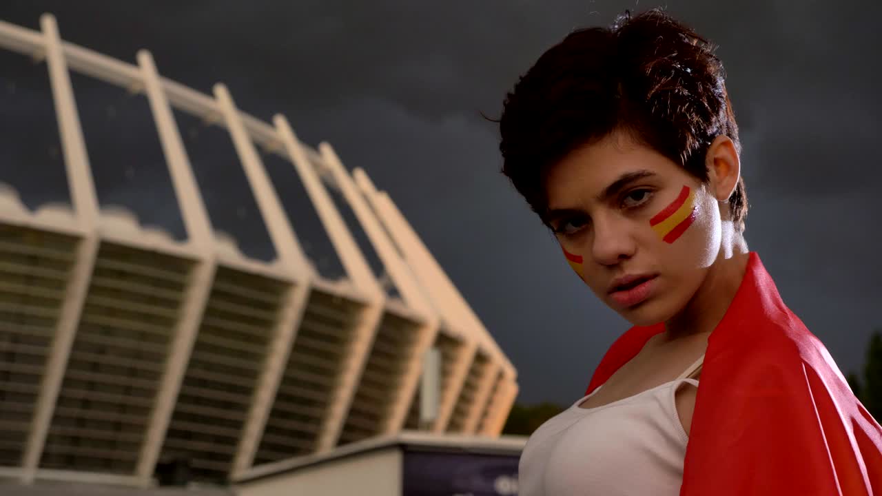 스페인에서 젊은 갈색 여자 축구 팬의 초상화, 카메라를보고, 미소 짓고, 웃고, 배경에 경기장 50fps