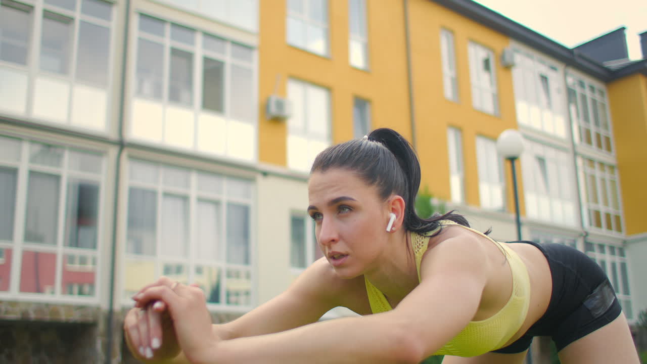 una mujer joven con auriculares realiza pendientes en el parque en el césped en el fondo de la ciudad.
