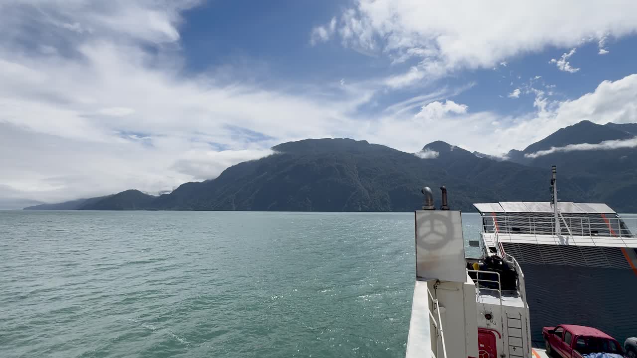 Handgehaltene Seitenansicht von einer Fähre, die Caleta Gonzalo verlässt, zeigt den dichten Regenwald, der in der chilenischen Patagonien auf die Fjordgewässer trifft.