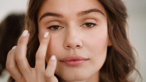 focused woman smears concealer on soft skin under eyes