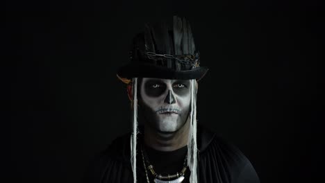 hombre siniestro con maquillaje de esqueleto de halloween girando la cabeza y mirando a la cámara, tratando de asustar