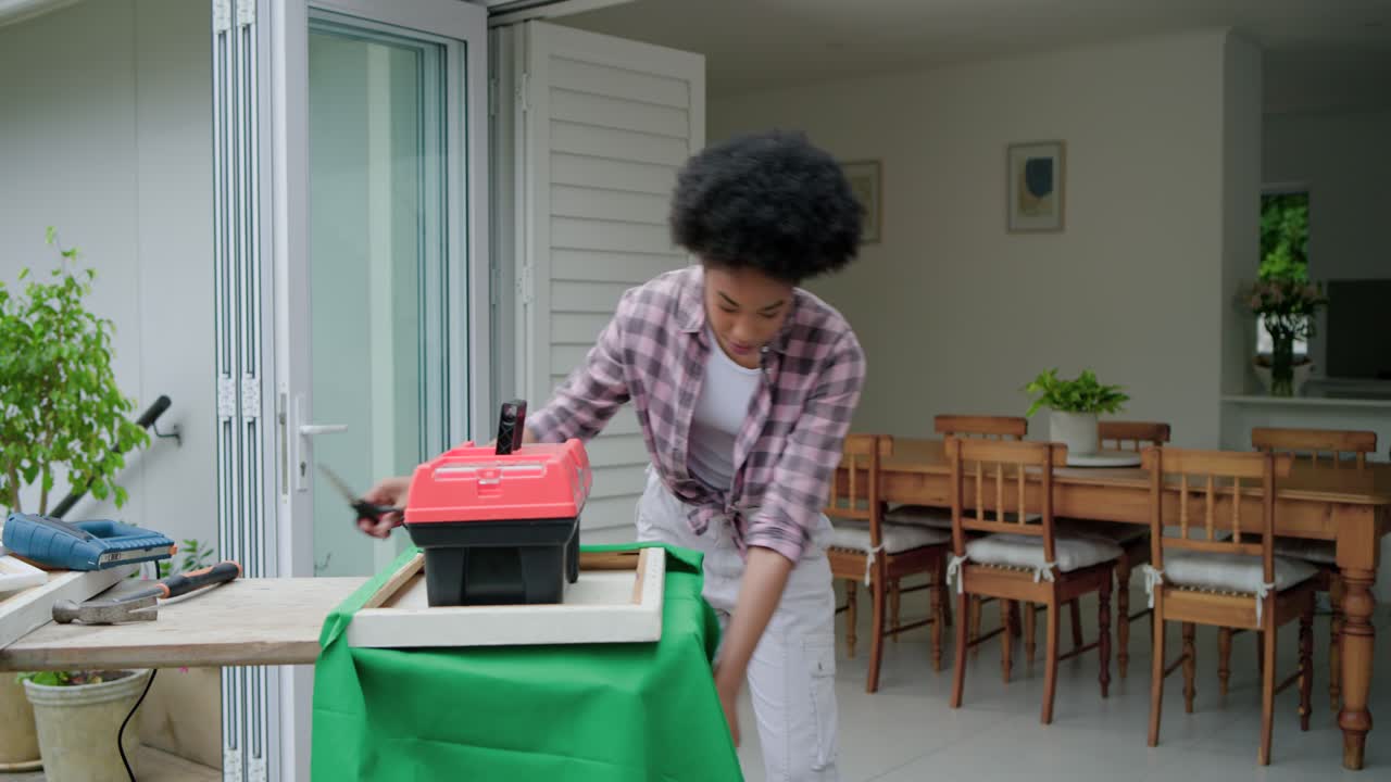Una donna stende un tessuto verde su una panca, appesantendo la struttura con una cassetta degli attrezzi e rifinendo i bordi per un progetto fai da te.