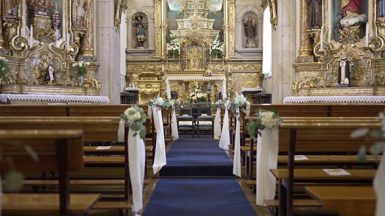 Interno elegante di una chiesa adornato con dettagli dorati e composizioni floreali, con una navata blu che conduce all'altare.