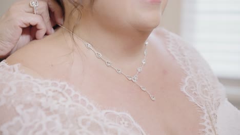 bride having her diamond necklace put on by her mother in slow motion