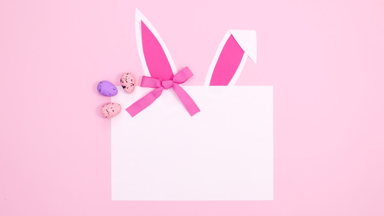 파스텔 분홍색 배경에 토끼 귀, 활 및 달을 가진 창의적인 부활절 종이 카드 메모.