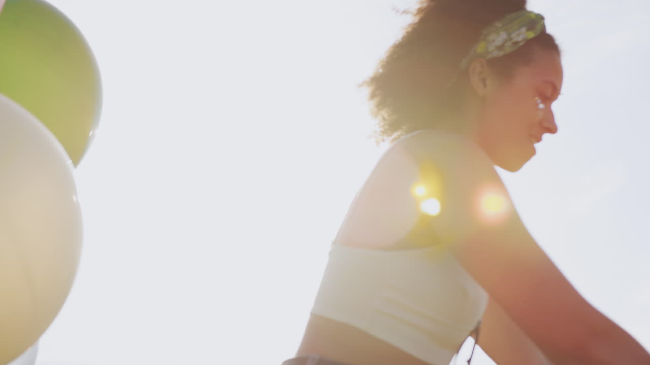 불타는 빛에 맞서 시골을 가로질러 풍선으로 장식된 자전거를 타는 젊은 여성