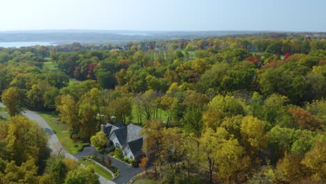 drone flies above large homes surrounded by autumn landscape on a golf course