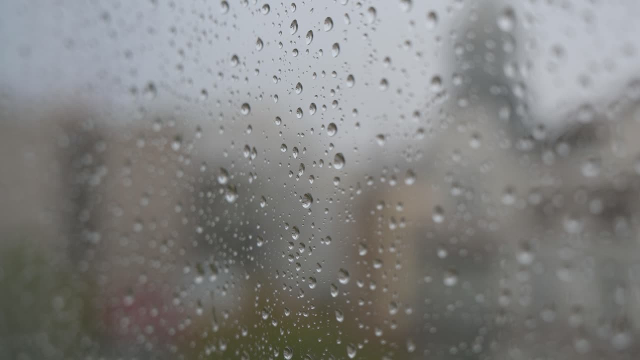 Close-up shot of raindrops on a window looking out to gloomy, overcast weather