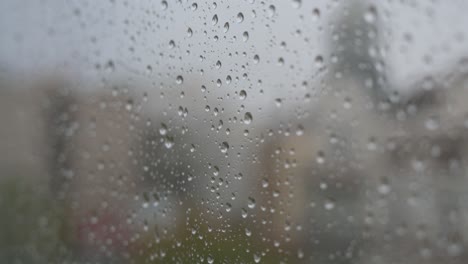 Close-up-shot-of-raindrops-on-a-window-looking-out-to-gloomy,-overcast-weather