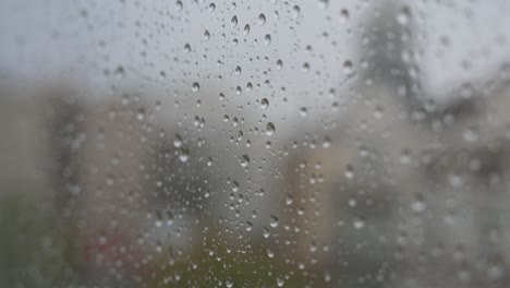 close-up shot of raindrops on a window looking out to gloomy, overcast weather