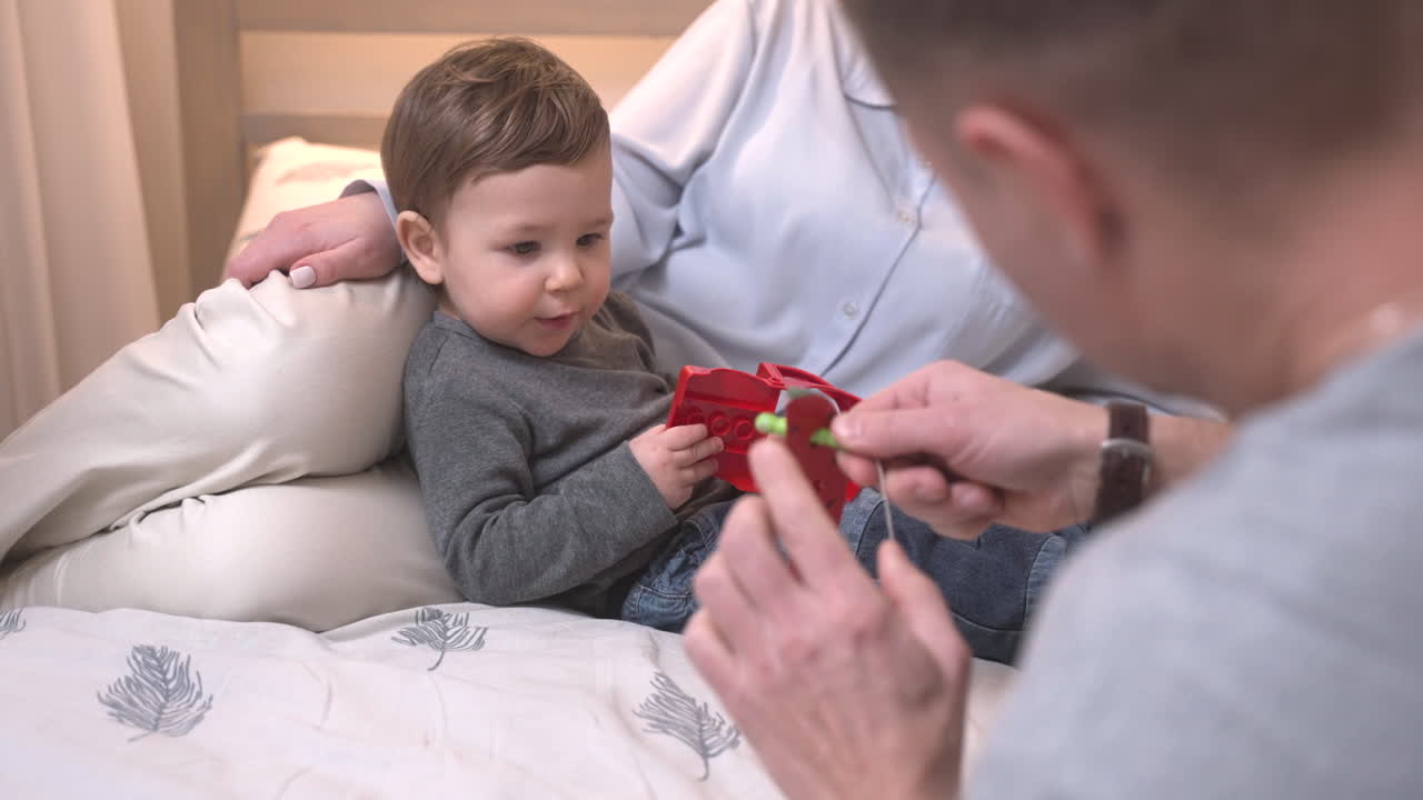 Baby Lying On His Mother's Lap On The Bed While Playing With His Father