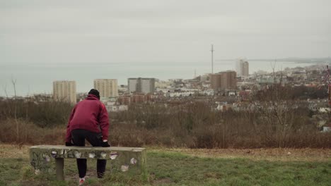 white man in red hoodie sits on bench and looks over brighton, seaside city