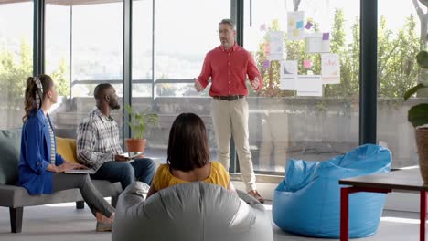 Caucasian-businessman-discussing-with-his-colleagues-over-memo-notes-on-glass-window-at-office