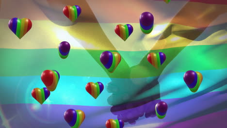 Animation-of-rainbow-hearts-and-flag-over-people-holding-hands