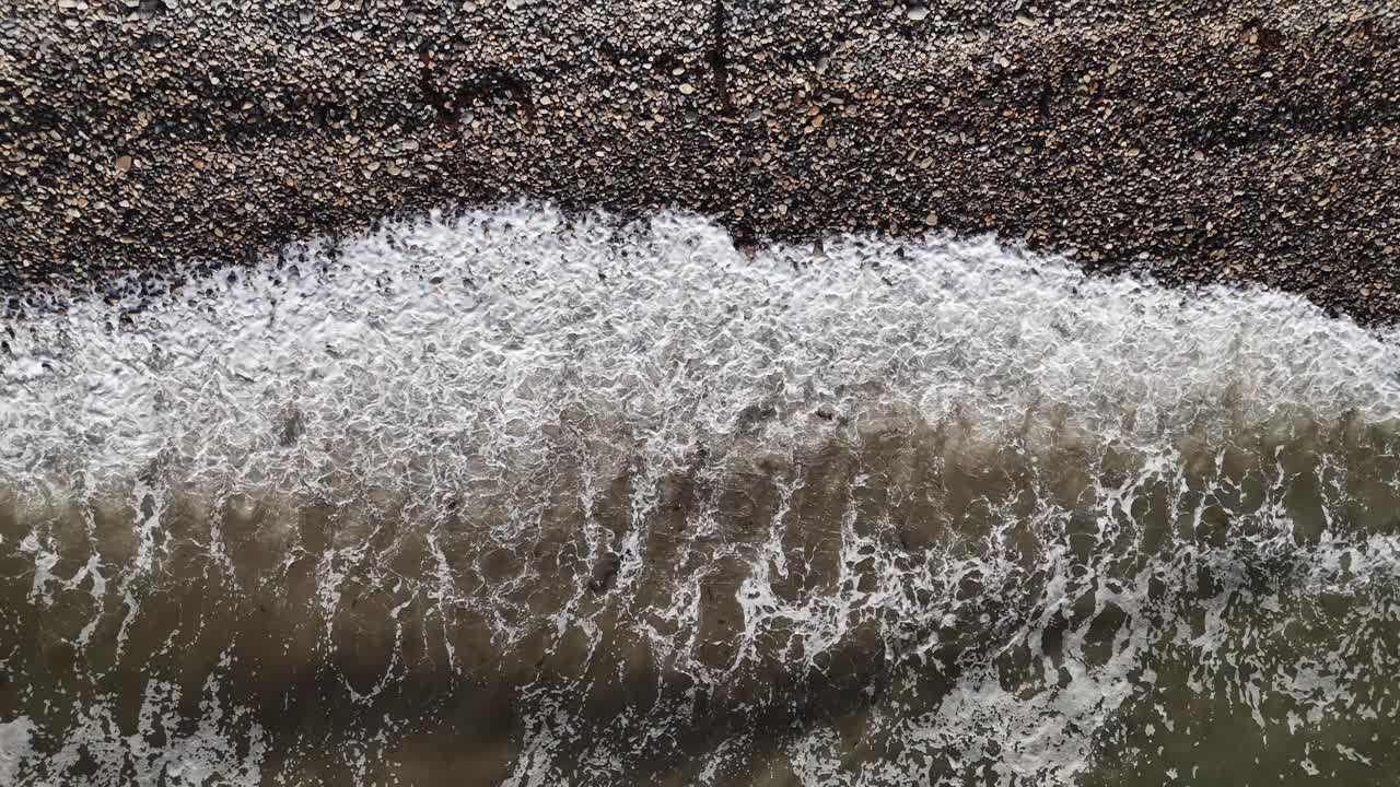 A stunning 4K aerial of San Pedro's pebble beach with waves gently crashing ashore. Ideal for nature, travel, or relaxation visuals with a peaceful, coastal vibe.