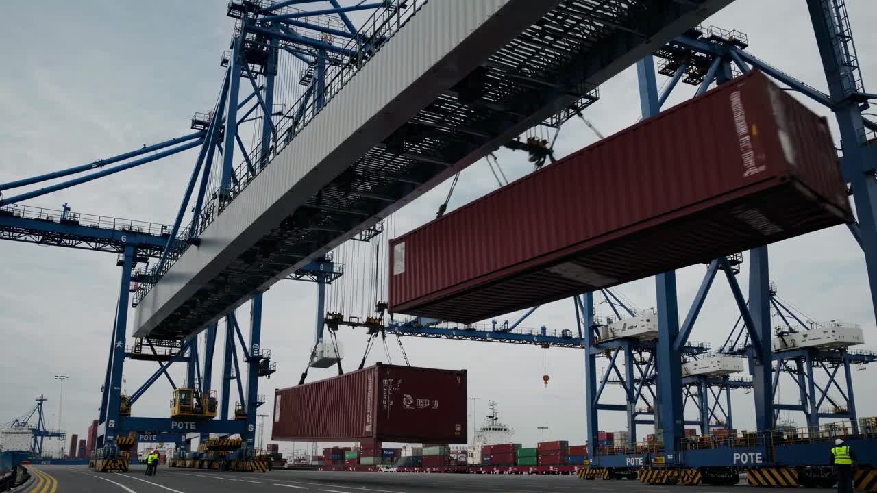 Low-angle video shot of a busy shipping port, capturing cranes lifting containers