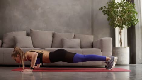 mujer joven sana en ropa deportiva haciendo flexiones en la alfombra de fitness frente al sofá. mujer joven haciendo ejercicio en casa. vista lateral