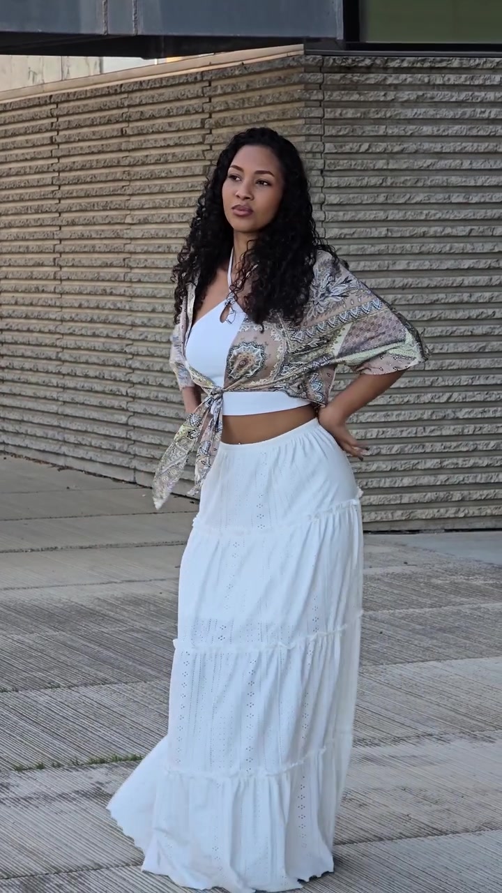 Uma mulher alegre está dançando ao ar livre com um traje de verão elegante e moderno sob sol forte.