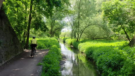 following a cyclist riding under an old stone train arch bridge