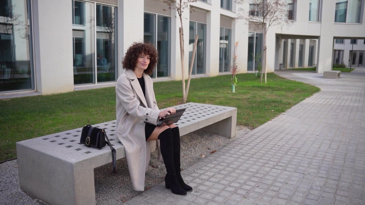 Una giovane donna seduta all'aperto che usa un laptop in un cortile moderno ed elegante