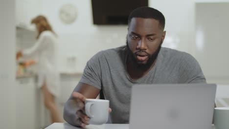 Hombre-Negro-Concentrado-Trabajando-Con-Computadora-Portátil-En-La-Cocina-Abierta.