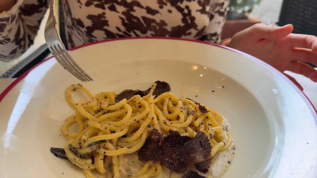 Primo piano di una persona che avvolge spaghetti con tartufo fresco e salsa alla panna.