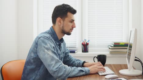 joven hombre de negocios trabajando en la computadora en una oficina moderna con estilo. computadora, teléfono y taza en la mesa. filmado en 4k