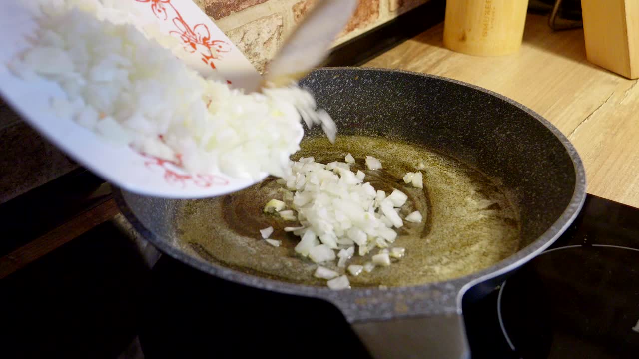 Chef is adding diced onions to a pan with olive oil