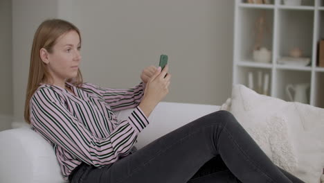 adult woman is browsing social nets in smartphone lying on couch at home swiping and scrolling