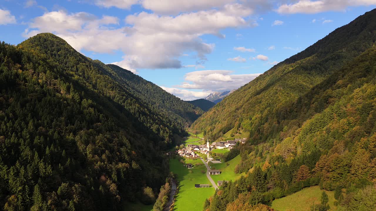 Zali Log village framed by autumn forest and distant peaks under warm daylight, Orbiting aerial tracking left