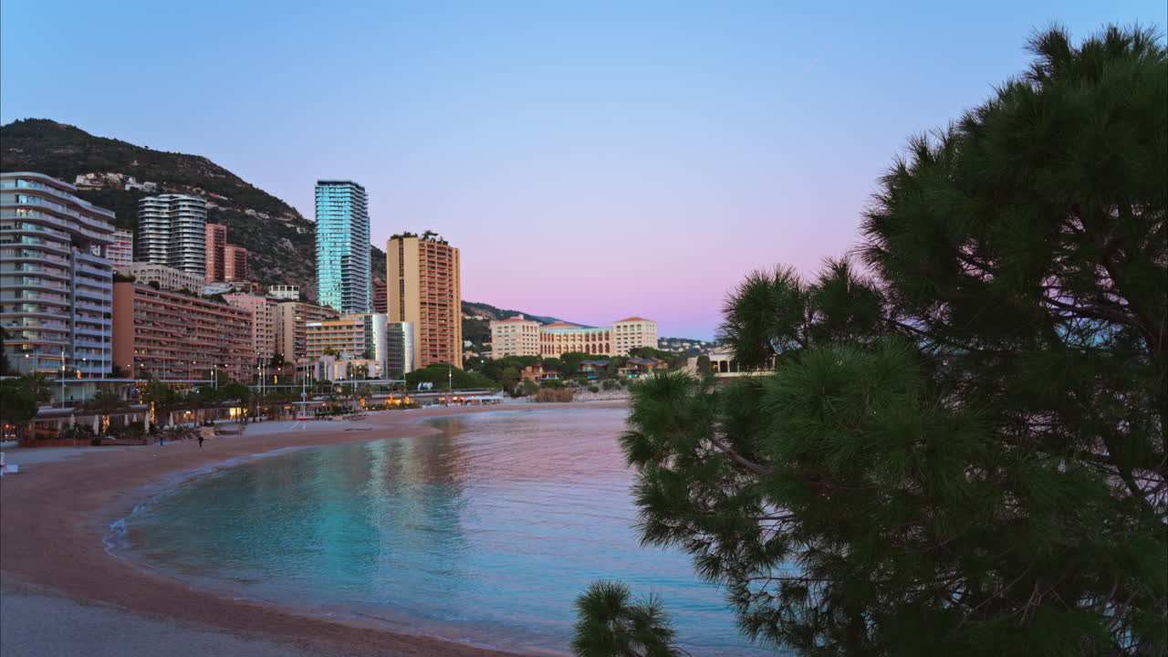 Vista della spiaggia di Larvotto a Monaco al tramonto con lo skyline della città sullo sfondo