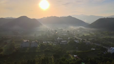 aerial 4k drone footage flying over a small rural village in a valley between two mountain ranges in khao yai, thailand during sunset