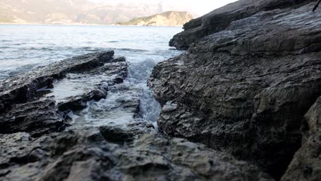 Waves-crashing-into-rocks-near-Budva-old-town-on-the-coastline-of-Montenegro-on-the-Adriatic-coastline-on-a-sunny-sunset-afternoon