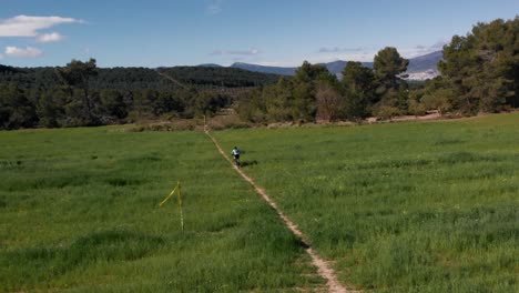 Mountain-biker-rides-through-green-meadow-in-springtime