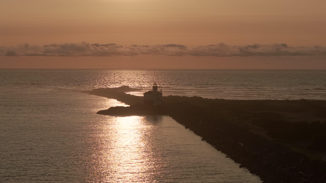 Silhouette of lighthouse in Bandon at the Southern Oregon Coast. Reflection of sun in the water. Drone view.