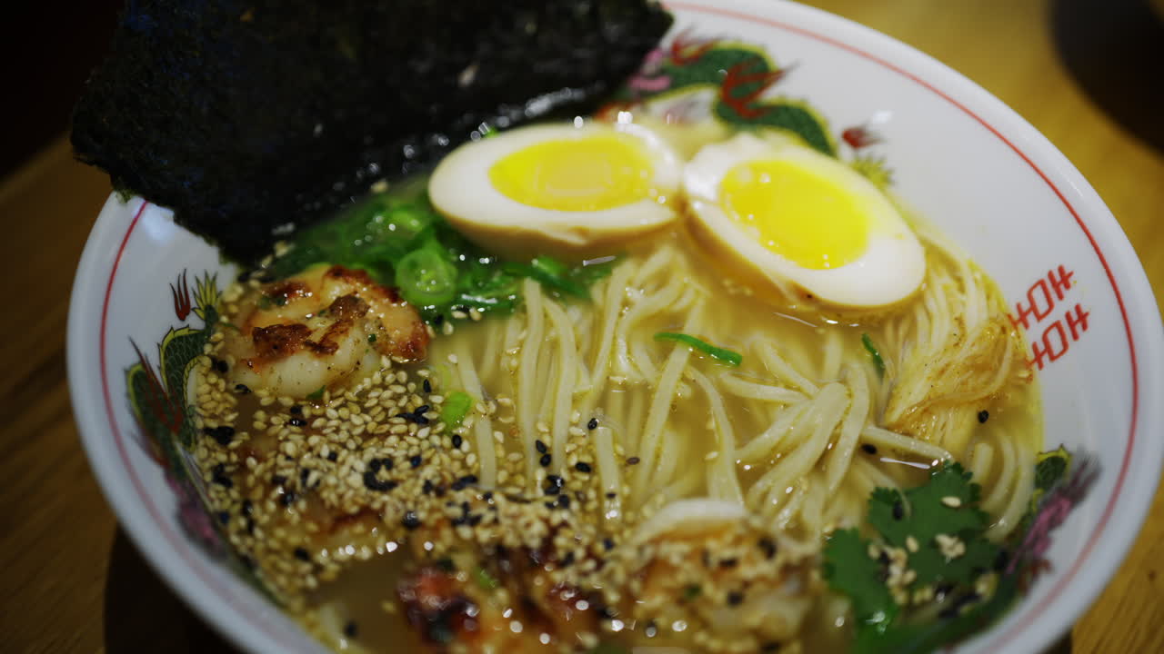 Deliziosa ciotola di zuppa di ramen con uovo barzotto, semi di sesamo, erbe aromatiche e alga marina.